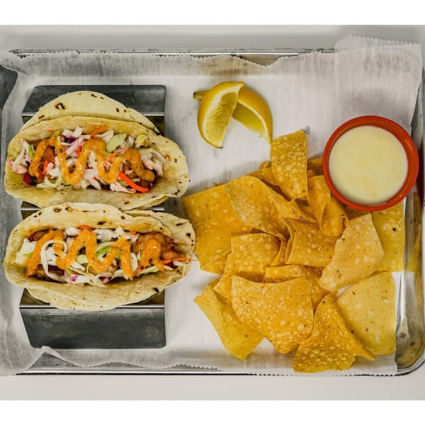 Two Hops N Guac tacos with slaw and sauce, served with tortilla chips, queso, and lemon wedges.
