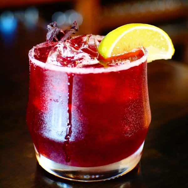 Hops N Guac's vibrant red cocktail with ice, a lime wedge, and a salted rim.
