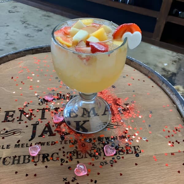 Fruity margarita with a strawberry garnish and heart-shaped confetti on a wooden barrel.