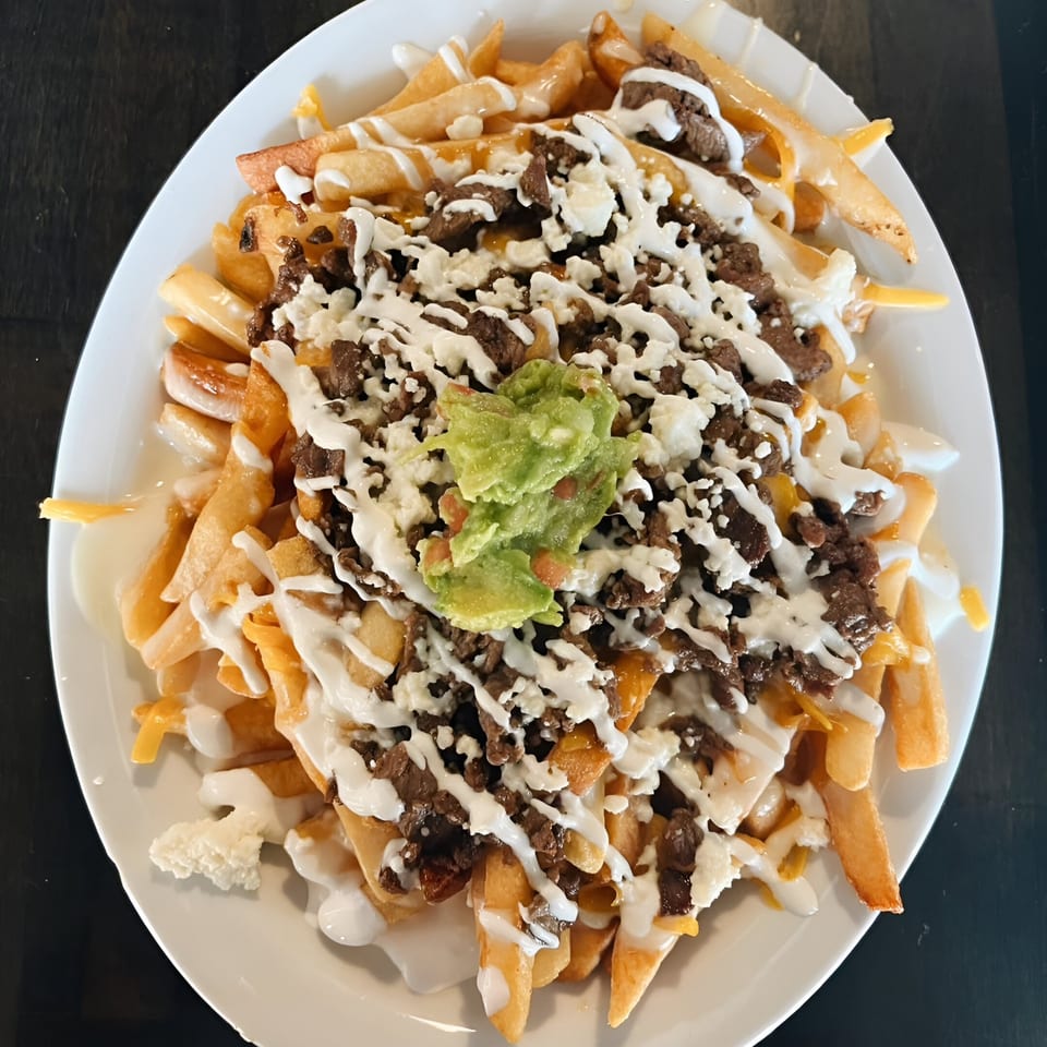 Hops N Guac's carne asada fries, topped with guacamole, sour cream, and cheese.
