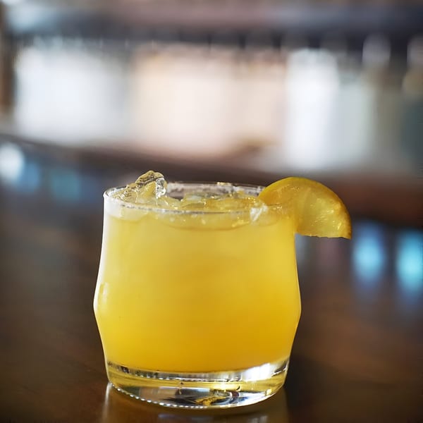 A Hops N Guac margarita with a salted rim and lime wedge on a dark wooden bar.